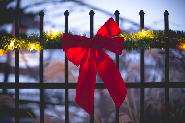 Red festive ribbon on the fence decorated with a coniferous garland