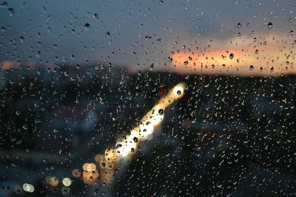 Raindrops on the glass against the background of a glowing city