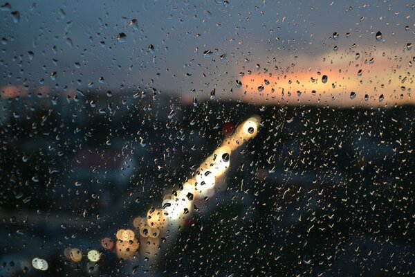 Gotas de lluvia en el cristal en el fondo de la ciudad brillante