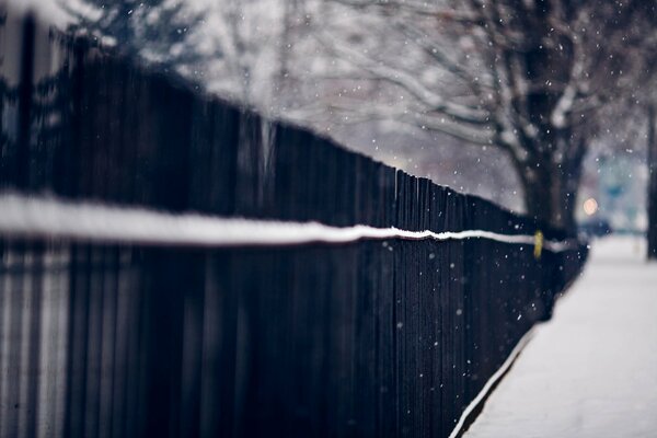 Langer schwarzer Zaun entlang einer verschneiten Straße