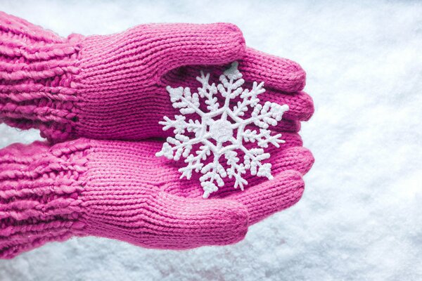 Schneeflocke in den Händen in rosa Handschuhen
