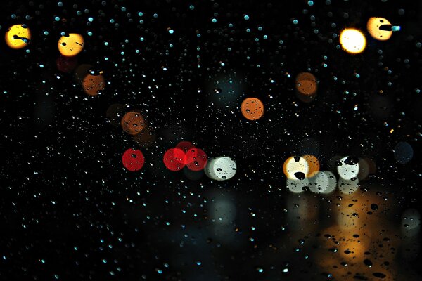 Pequeñas gotas de lluvia en el vidrio con luces de la ciudad
