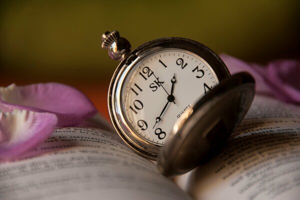 Horloge sur le livre. Pétales de rose sur le livre