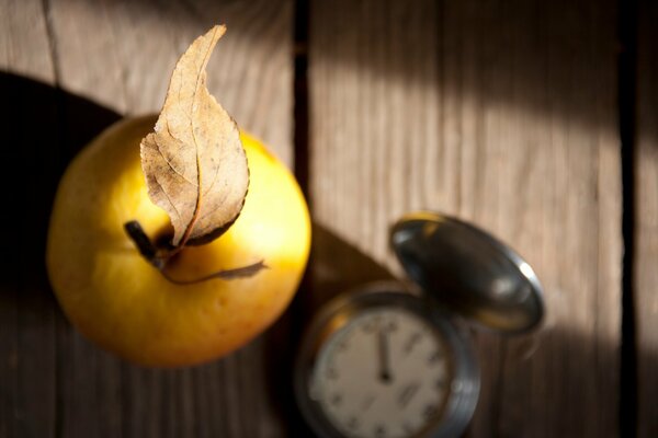 An apple with a leaf and a clock on a wooden table