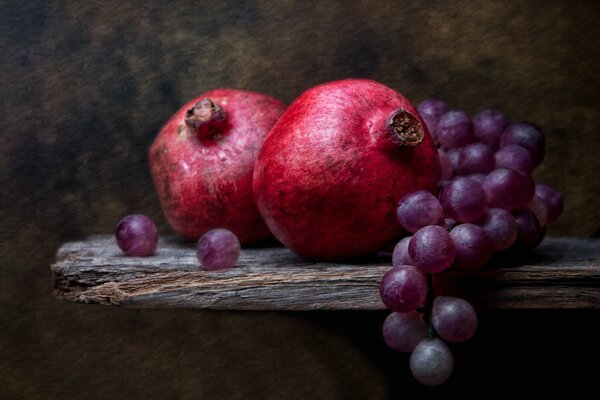 Still life Two pomegranates and a bunch of grapes on the table 