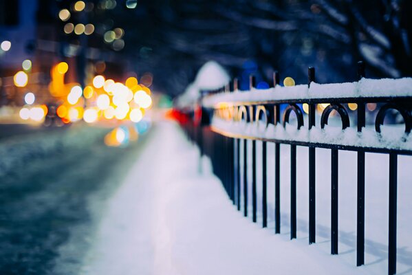 A snow-covered fence by the road. blurred background