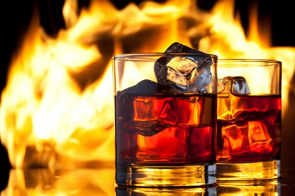 Two glasses of whiskey with ice on the background of fire