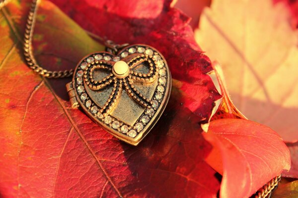 Брелок в виде сердца украшенный бантом лежит на осеннем листе