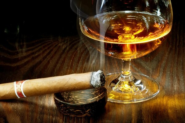 Cigare avec la maison à côté du cognac dans un verre