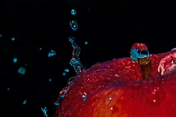 Wassertropfen brechen über einen roten Apfel