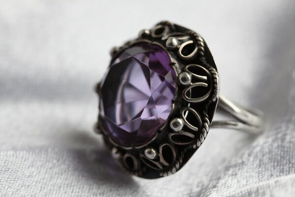Кольцо из серебряного металла с фиолетовым камнем на фоне серой ткани