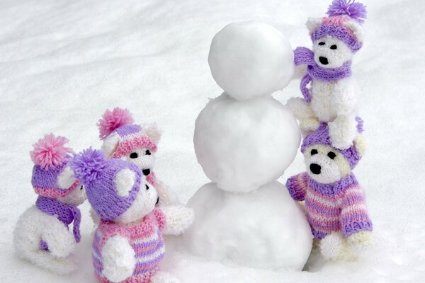Knitted teddy bears on a snowman in purple hats
