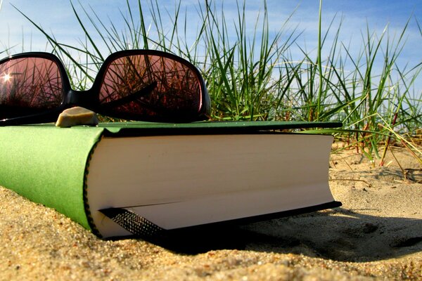 Occhiali da sole e libro lasciati sulla spiaggia sabbiosa in estate