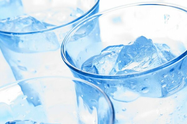 Три прозрачных стеклянных стакана с прозрачной жидкостью и льдом в голубых тонах