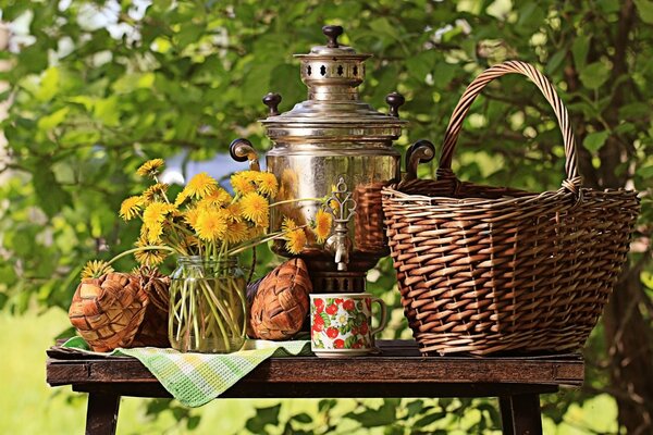 Still life del tavolo con samovar, cesto, verde sullo sfondo della natura