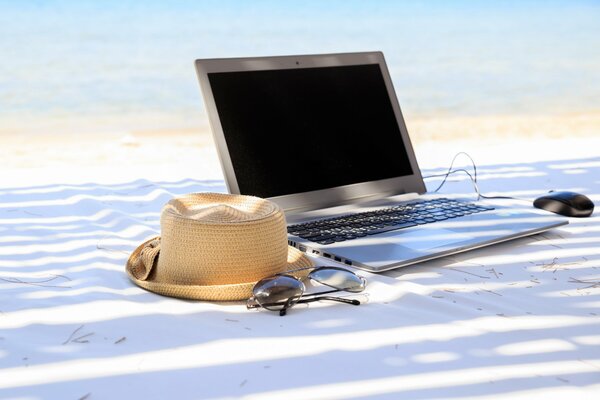 Laptop and hat are lying on the white sand