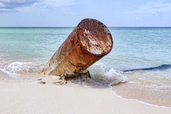 Ein Metallrohr, das aus dem Sand am Meer ragte