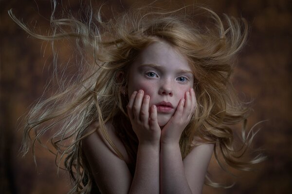 Retrato de una niña pelirroja que apoya sus mejillas con las manos