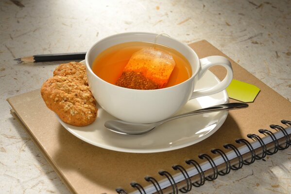 A cup of tea with cookies on a notepad with a pencil