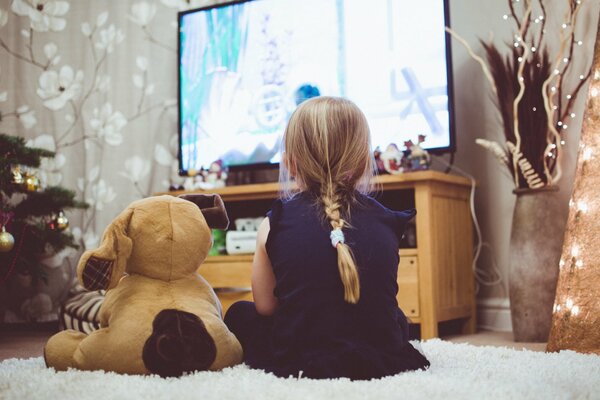 Bambina con giocattolo sul letto guardando la TV a Capodanno