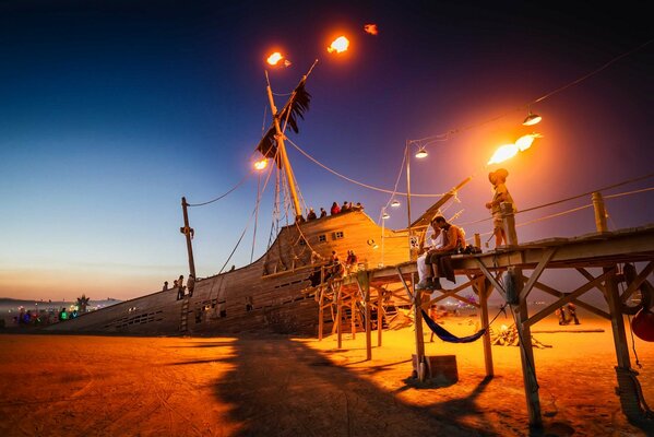 Bei Sonnenuntergang sinkendes Schiff mit brennendem Mast und Menschen an Deck