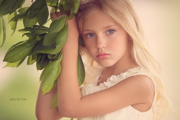 The girl is holding on to a branch with green leaves