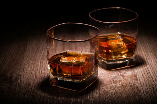 Zwei Gläser Whisky mit Eis auf einer Holzplatte