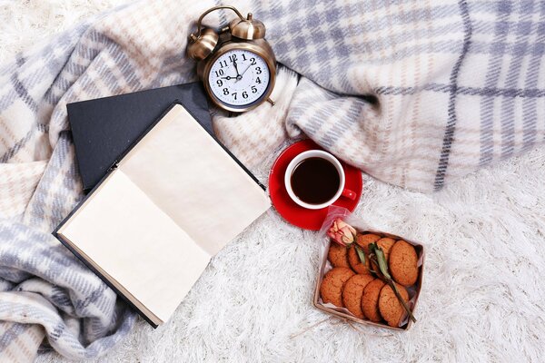 El despertador descansa sobre una manta junto a un libro y un café