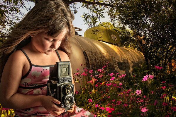 Ragazza con una macchina fotografica sullo sfondo di un prato fiorito e una cisterna