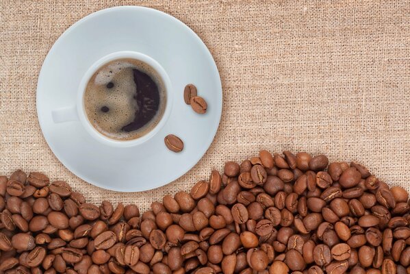 A cup of coffee on a saucer and coffee beans