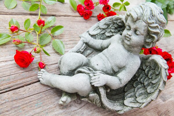 Figura de ángel Cupido en la mesa con rosas rojas
