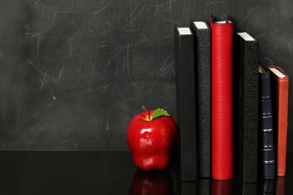 Red and black diaries on a black background. a red apple on a black shelf