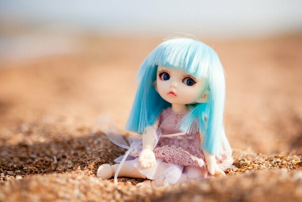 Eine sitzende Puppe im Sand mit blauen Vlos