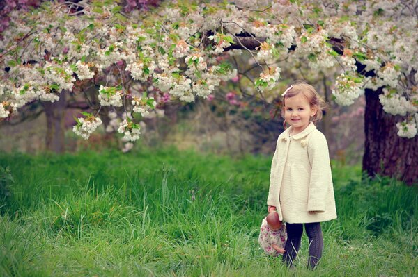A girl with a doll on the background of a flowering tree