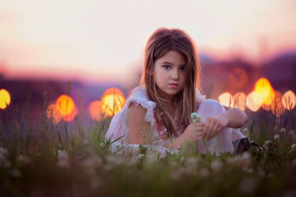 Jeune fille assise sur le terrain, avec des fleurs à la main