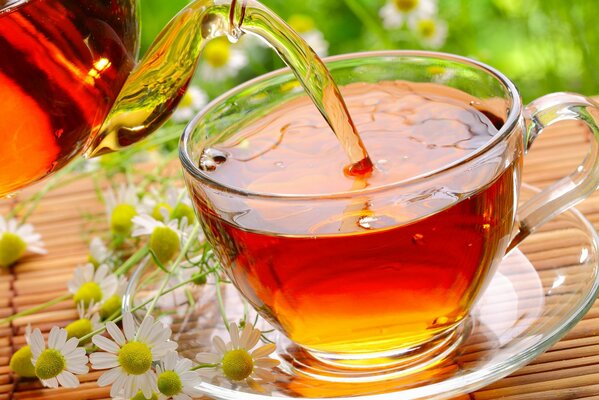 A teapot pours tea into a cup against a background of daisies