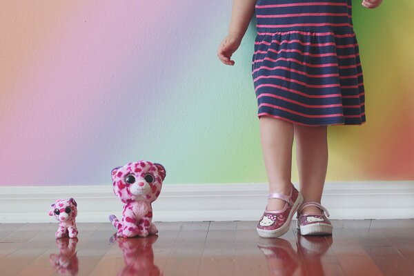 Две игрушки рядом с ногами девочки около стены