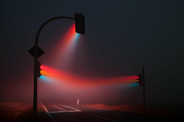 Los semáforos con sus rayos de color dispersan la niebla de la carretera nocturna