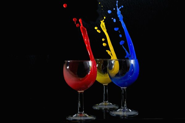 Tre bicchieri da vino con liquido multicolore che fuoriesce su sfondo nero