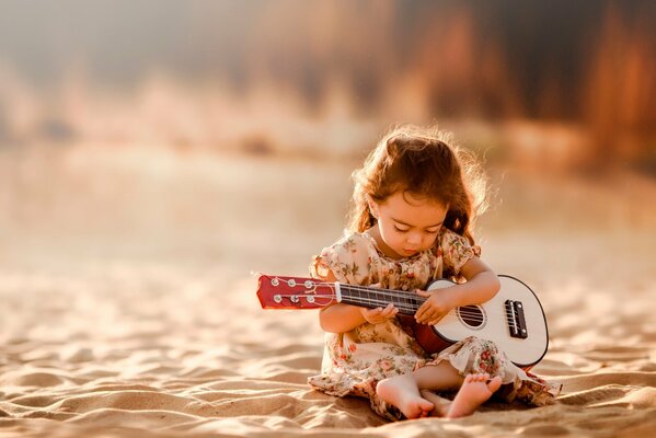 Девочка на песке с гитарой играет мелодии от души