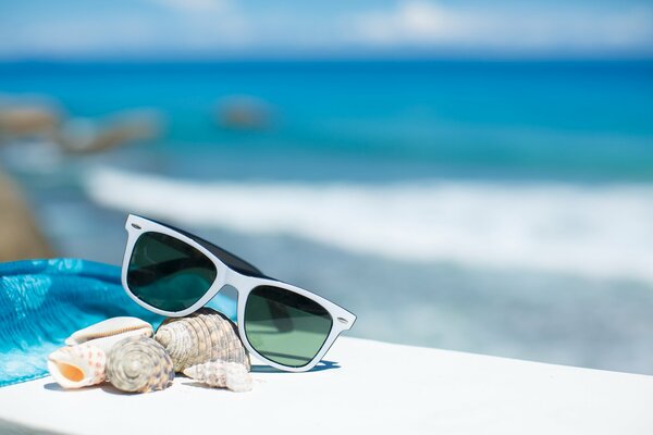 Sonnenbrille, Muscheln, blauer Pareo auf einer weißen Bank. Das Meer