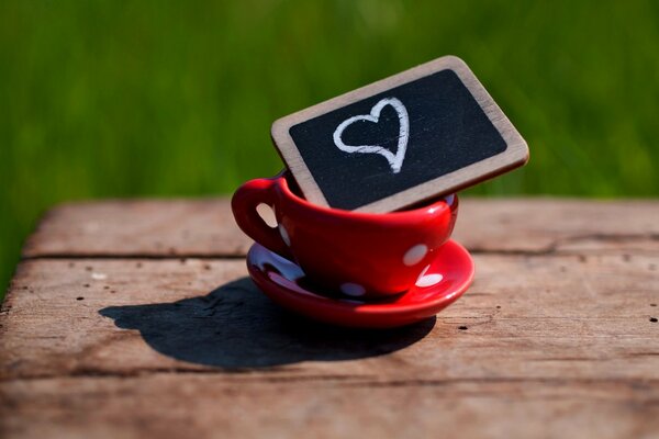 A red cup with white peas on a saucer with a plaque, a heart on a plaque with chalk