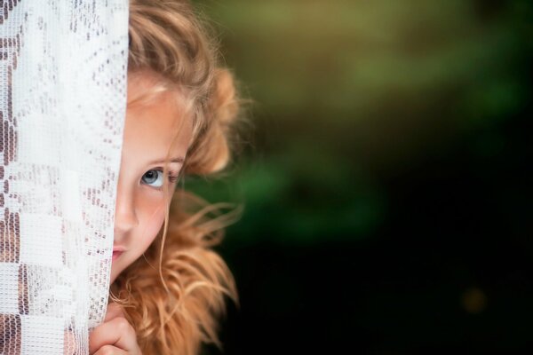 Photo of a girl peeking out from behind a curtain