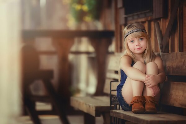 Mała dziewczynka z blond włosami siedzi na drewnianej ławce