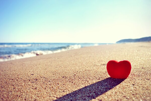 Ein rotes Herz ist am Strand im Sand vergraben