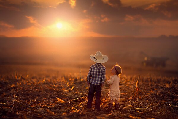 Ein Junge und ein Mädchen im Feld auf dem Hintergrund eines herbstlichen Sonnenuntergangs