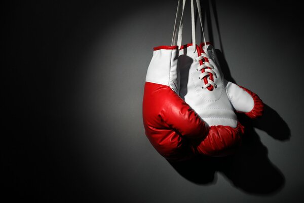 Rot-weiße Boxhandschuhe hängen an einer schwarzen Wand