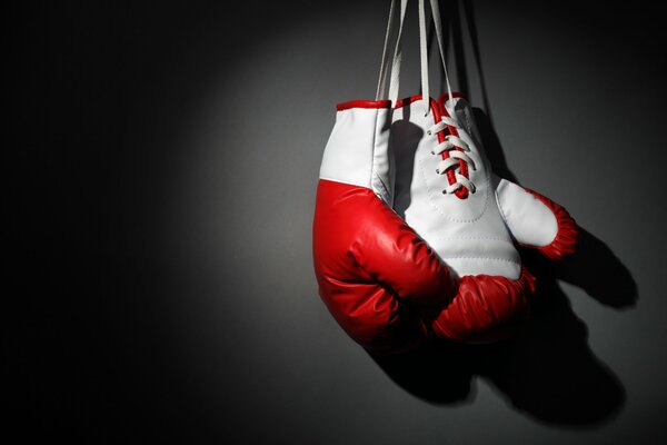 Red and white boxing gloves hang on a black wall