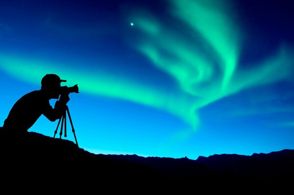 Силуэт фотографа снимающего северное сияние в ночи