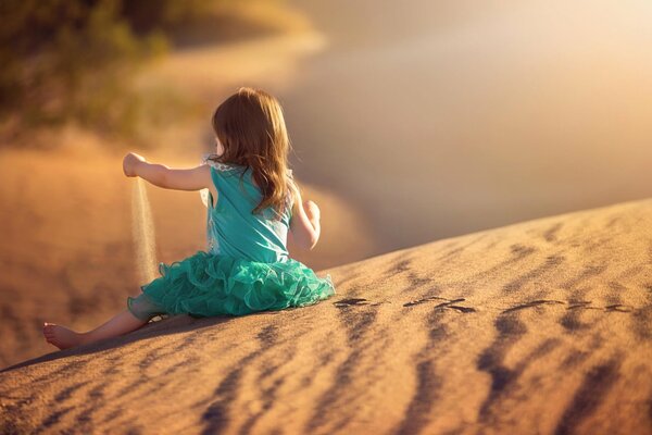 Девочка в бирюзовом платье играет с песком